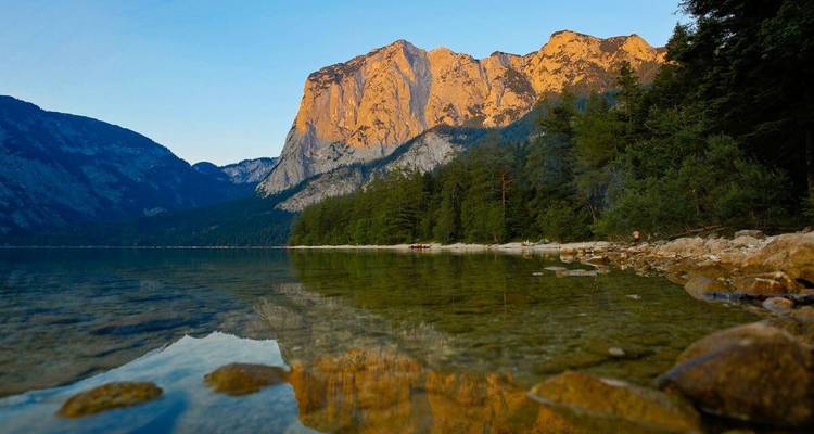 A tranquil lakeside scene with dramatic cliffs at sunset.