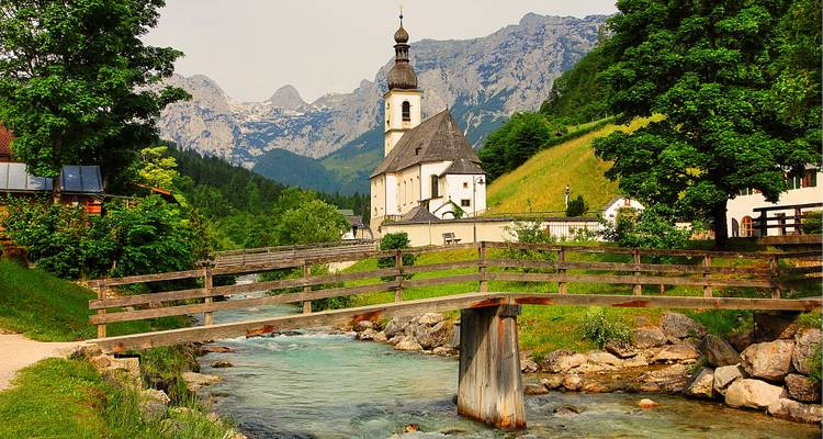 Un charmant village alpin avec une église au bord d'un ruisseau entouré de montagnes.