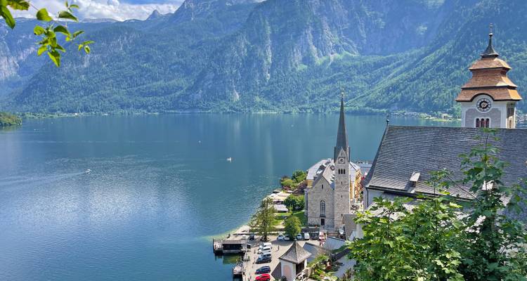 Panoramic view over Hallstatt village, church spire and deep blue lake framed by high cliffs.