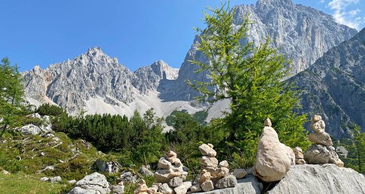Stone cairns stacked on grassy slope with dramatic rocky peaks behind.