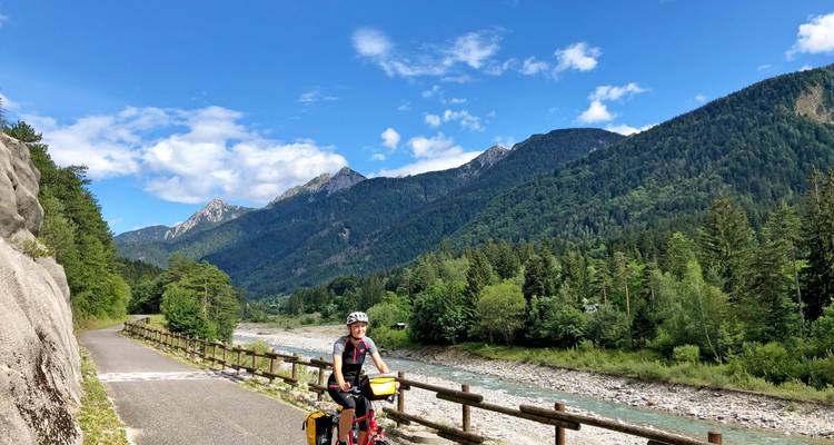 Radfahrer auf einem malerischen Bergpfad mit einem Fluss und Wald.