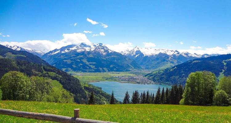 Panoramic view of a valley with snow-capped mountains and a lake.