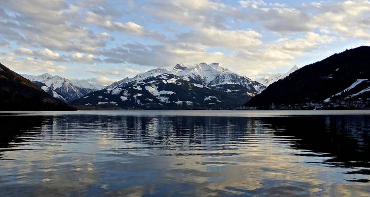 Reflet de montagnes enneigées dans un lac sous un ciel nuageux.