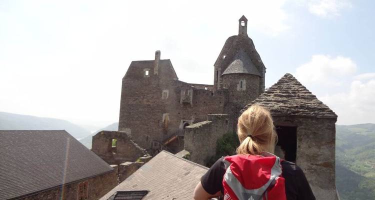 Personne avec un sac à dos debout devant les ruines d'un château médiéval.