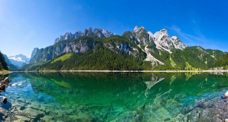 Un lac alpin turquoise reflétant des montagnes rocheuses et des arbres.