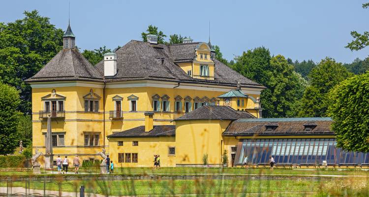 Yellow baroque-style building with people walking in a garden.