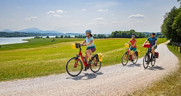 Three people cycling on a gravel path through open fields.