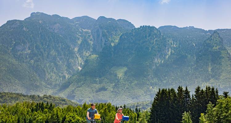 Two people cycling on a path surrounded by mountains.