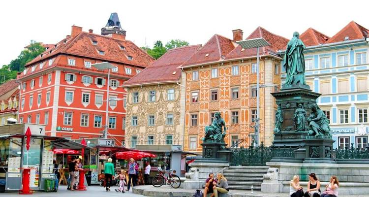 A lively city square with historical buildings and people.