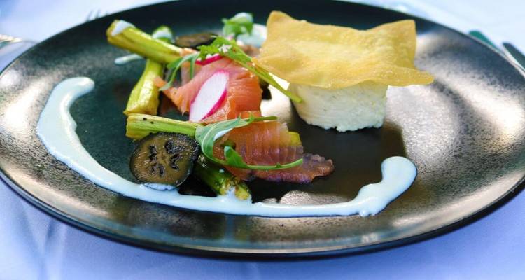A gourmet dish with smoked salmon, asparagus, and cream on a black plate.