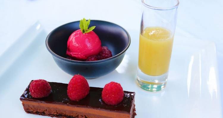 A gourmet dessert with raspberries and a glass of orange juice.