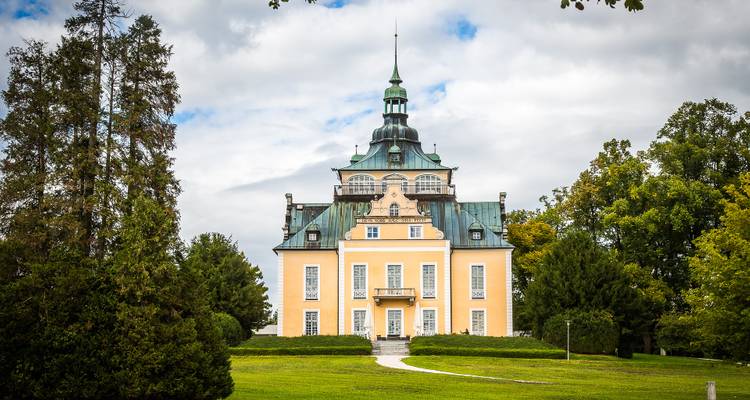 A picturesque building with a spire and ornate architecture set amidst greenery.