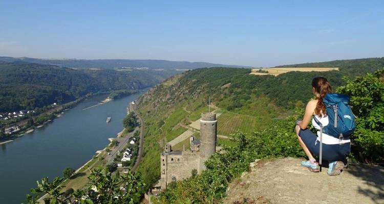 Wandelaar die uitkijkt over een rivier en kasteel vanaf een heuvel.