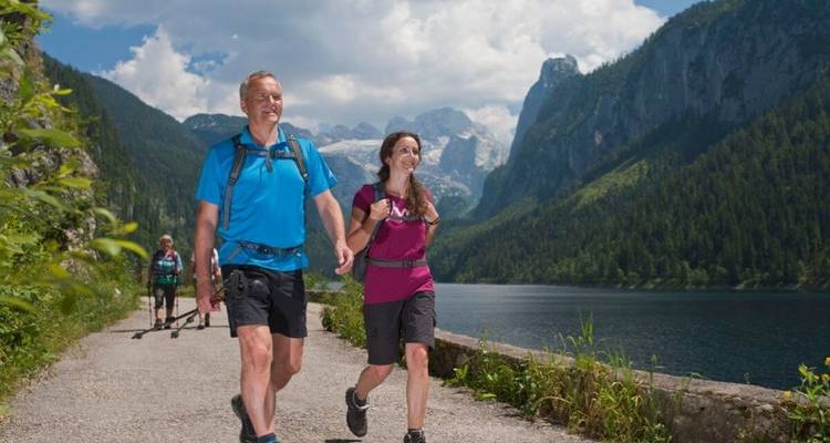 Des personnes marchant sur un sentier pittoresque au bord d'un lac avec des montagnes en arrière-plan.