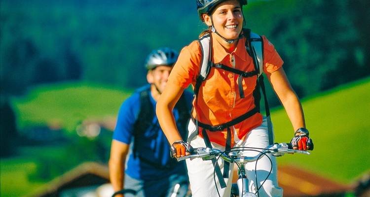 Smiling cyclist biking with greenery in the background.