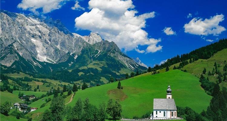 Une église pittoresque et des champs verts avec des montagnes imposantes.