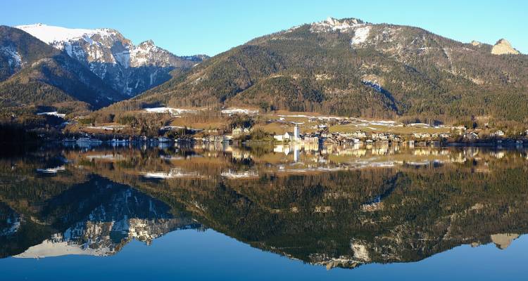 Vue panoramique d'une ville se reflétant dans un lac avec des montagnes enneigées.