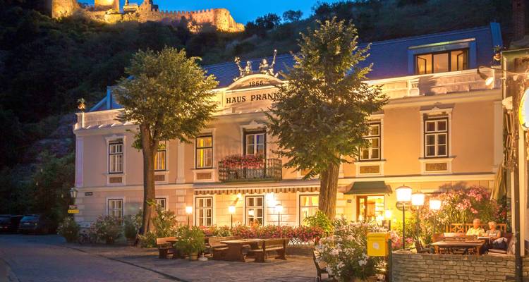 Bâtiment historique avec éclairages, arbres et ruines de château visibles la nuit