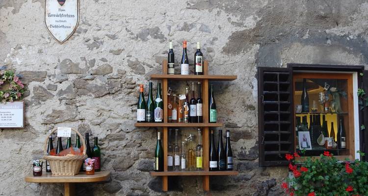 Mur orné d'étagères de bouteilles de vin dans un cadre de village pittoresque.