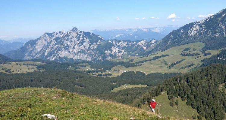 Une personne faisant de la randonnée sur une pente herbeuse avec une vue panoramique sur les montagnes.