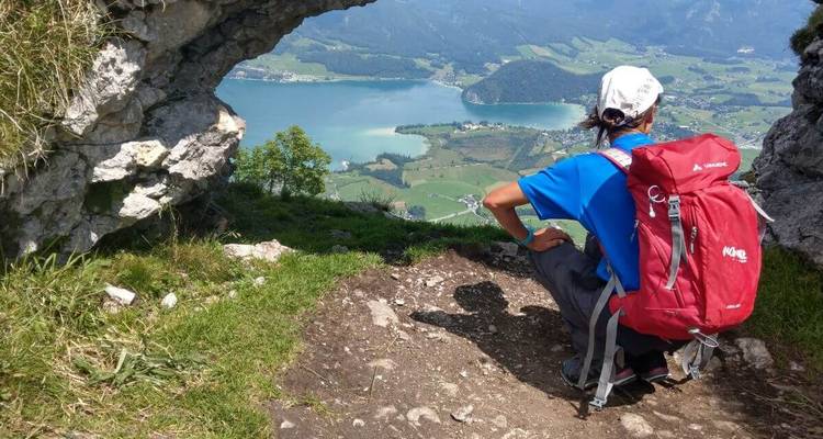 Un randonneur admirant la vue depuis une grotte de montagne surplombant un lac.