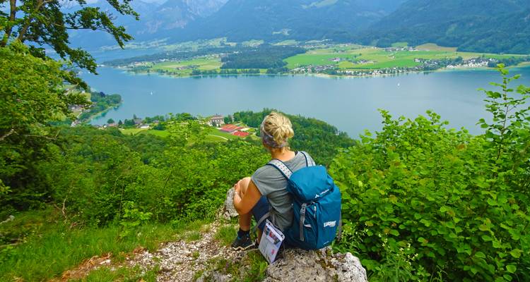 Een persoon die op een rots zit met uitzicht op een meer en dorp.