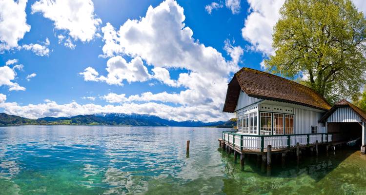 Een charmant uitzicht aan het meer met een boothuis en besneeuwde bergen op de achtergrond.