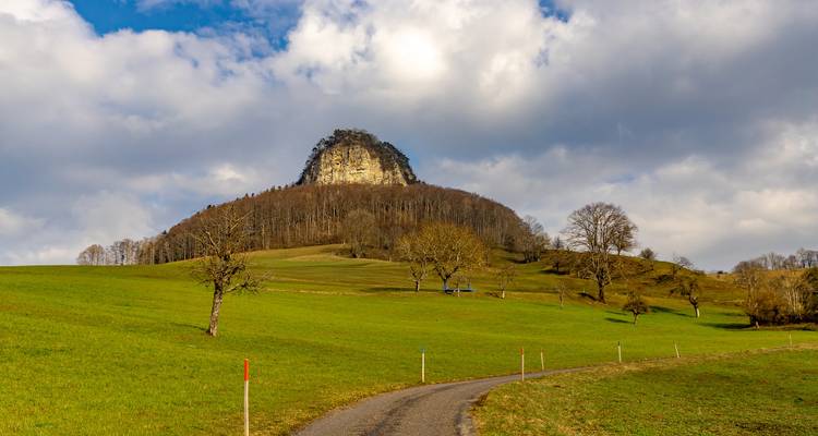 A rural landscape with a prominent rock hill and open grassy areas.