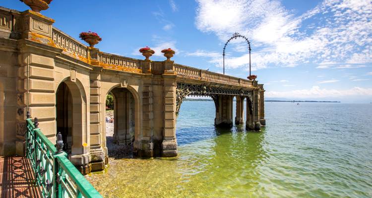 Puente histórico sobre un lago cristalino bajo un cielo azul brillante.