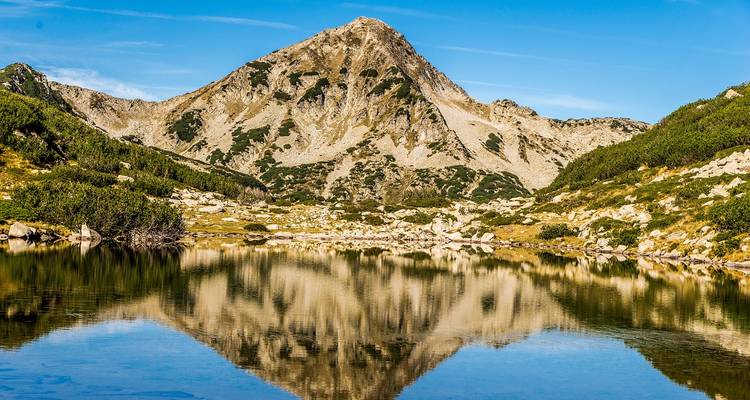 Mountain peak reflected in a tranquil lake surrounded by rugged terrain.