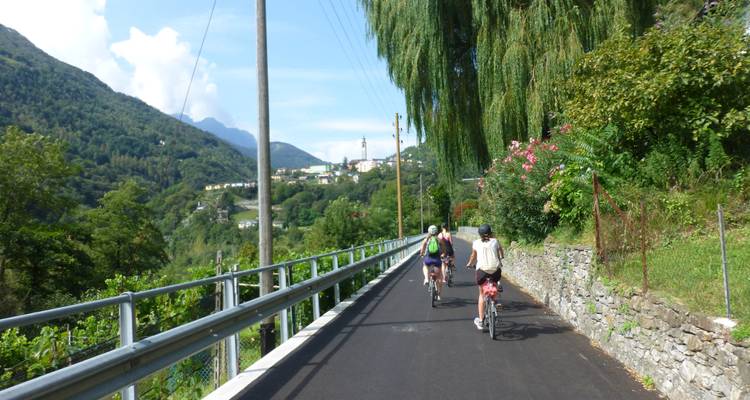 Cyclists on a paved path with lush green hills and a distant town.