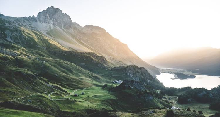 Paysage montagneux avec une route sinueuse, des vallées verdoyantes et un lac.