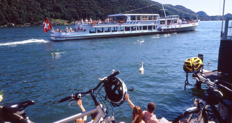 Gran ferry en un lago con personas y bicicletas en la orilla.