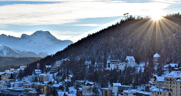 Ville enneigée dans les montagnes avec un soleil éclatant qui pointe par-dessus la crête.