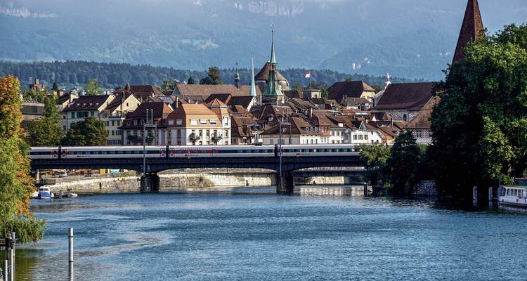 Une rivière avec un pont et un paysage urbain historique entouré de montagnes.
