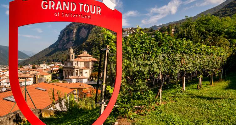 Panneau du Grand Tour de Suisse avec une église et des collines en arrière-plan.