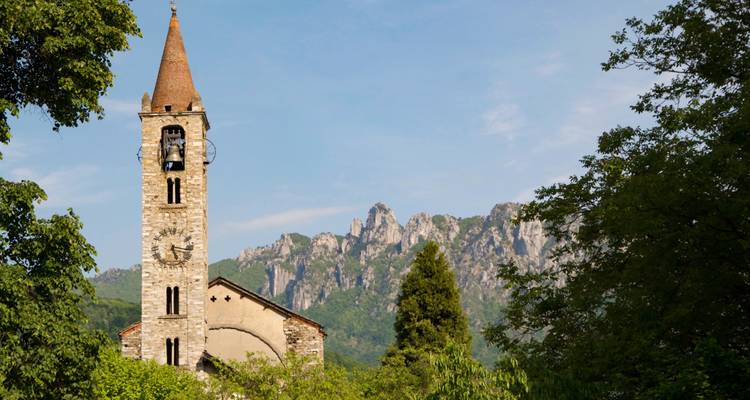 Église avec un clocher entourée de verdure et de montagnes.