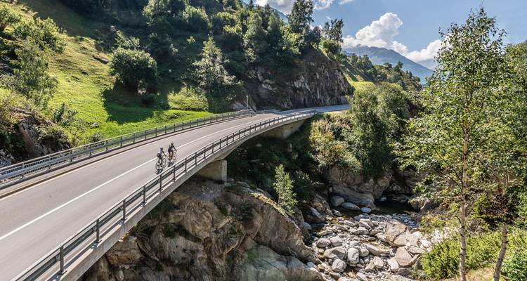 Dos ciclistas en un puente rodeado por un valle exuberante.