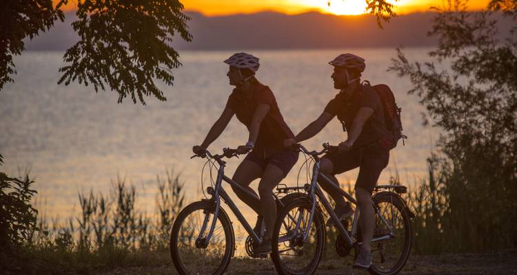 Dos ciclistas disfrutando de un paseo panorámico junto a un lago al atardecer.
