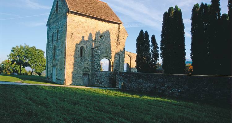 Stone chapel with arched windows casts long morning shadows across a grassy hilltop.