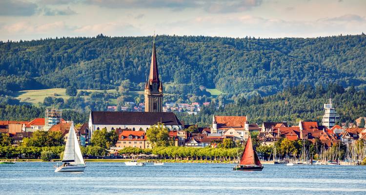 Boote, die auf einem See segeln, mit einer Stadt und einem Kirchturm im Hintergrund.
