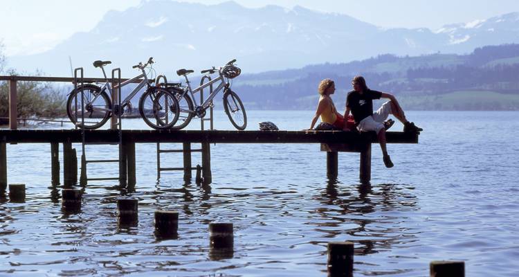 Couple assis sur une jetée en bois avec des vélos et des vues panoramiques.