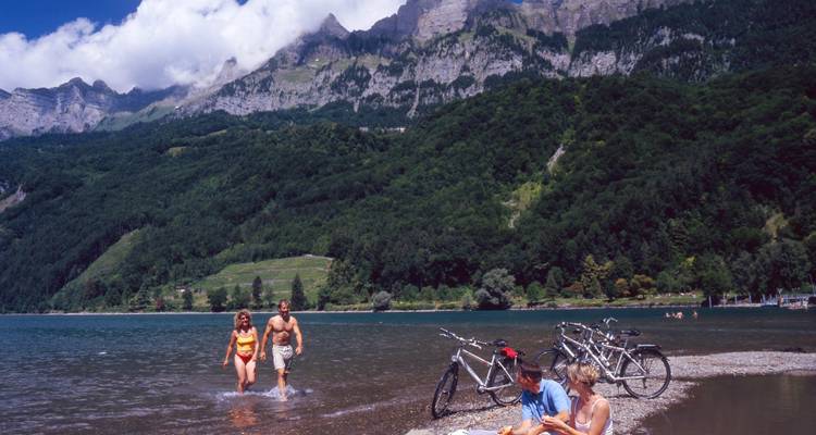 Des gens et des vélos près d'un lac avec des montagnes en arrière-plan.