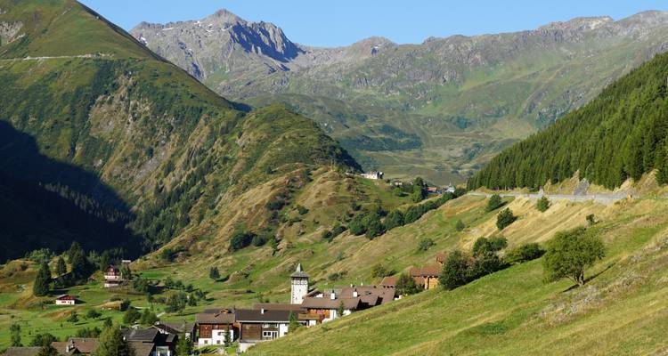 Village de montagne pittoresque avec des collines vertes environnantes et un ciel bleu clair.
