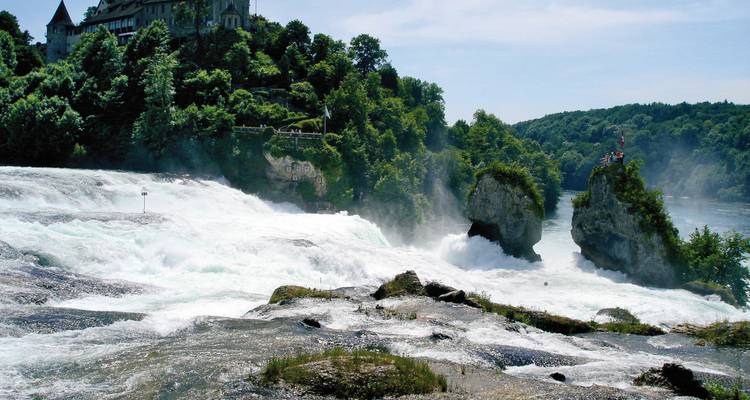Puissante cascade coulant sur les rochers avec un bâtiment semblable à un château en arrière-plan.