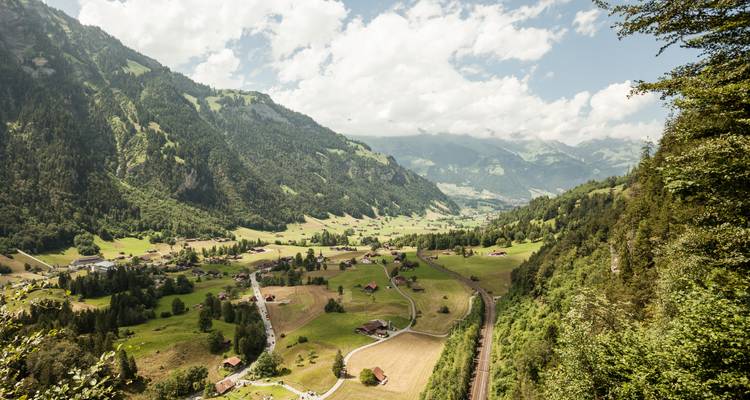 Vue panoramique d'une vallée luxuriante avec des montagnes et des villages.