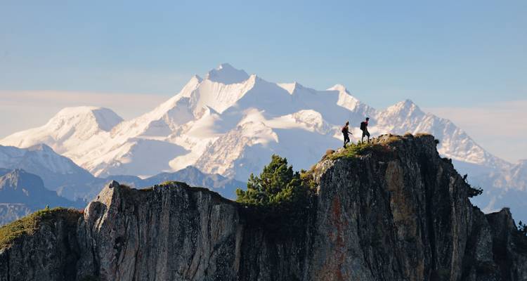 Des randonneurs debout sur un sommet rocheux avec des montagnes enneigées en arrière-plan.