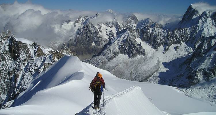 Persona haciendo senderismo en una cresta nevada con un telón de fondo montañoso dramático.