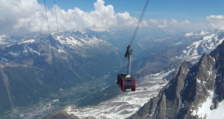 Teleférico volando sobre montañas nevadas y un valle verde.