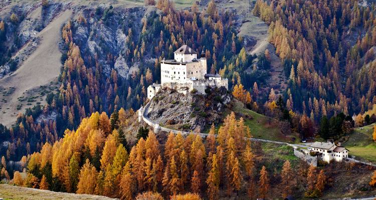Château sur une colline entouré d'arbres aux couleurs d'automne.
